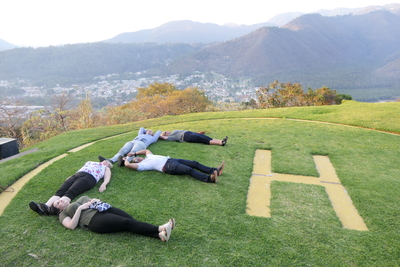 Five people lying on the grass creating an E next to an H in the grass