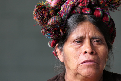 a woman with a colourful head dress sitting and looking off to the right hand of the screen